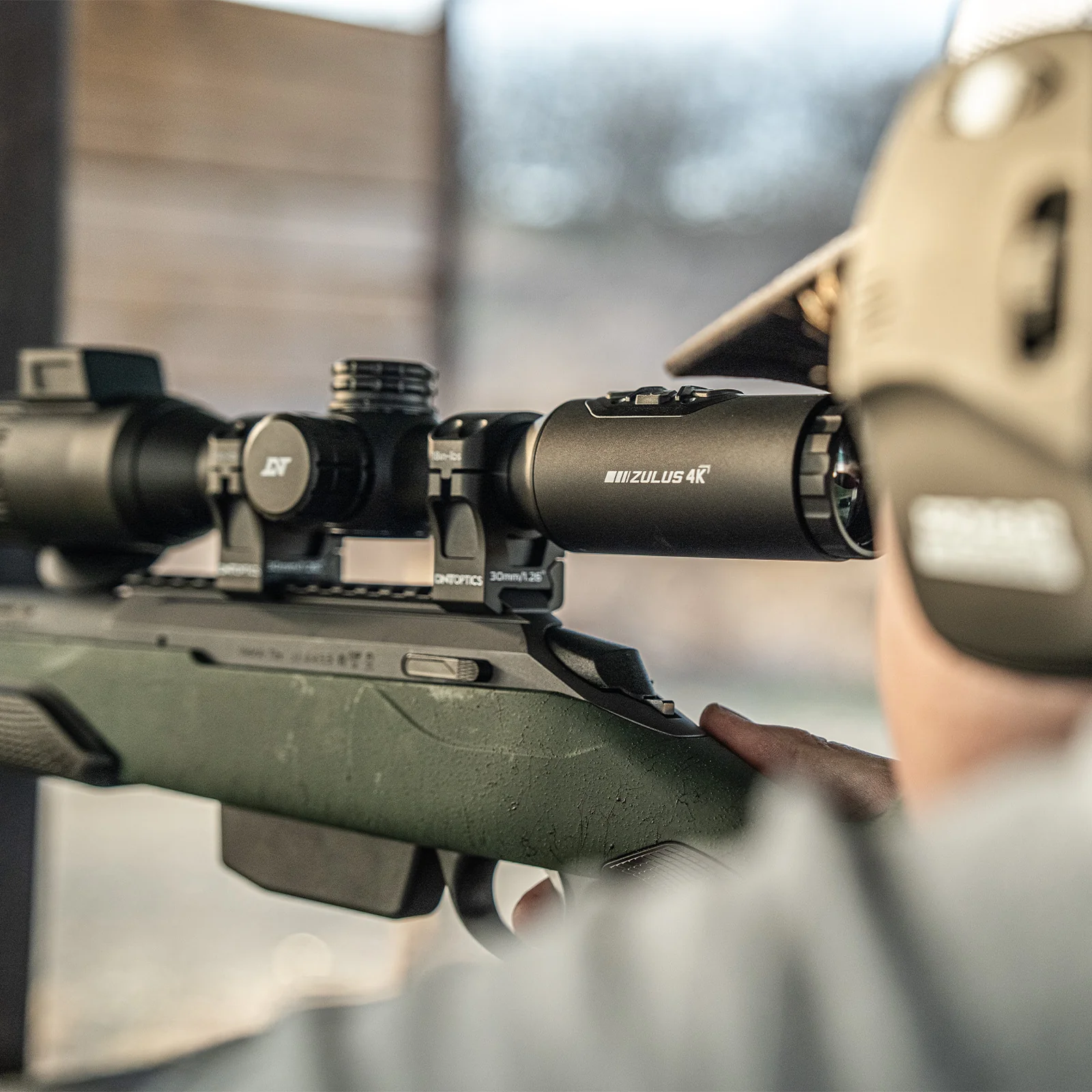 Shooter aiming a rifle mounted with a DNT Optics ZULUS 4K scope, over-the-shoulder view
